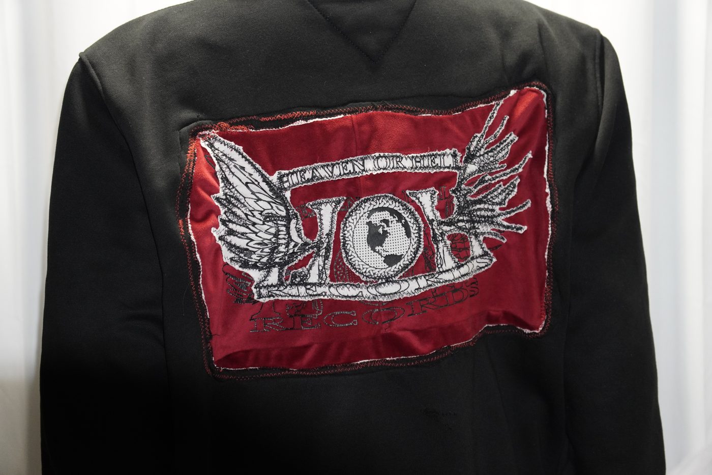Close-up of an embroidered Heaven or Hell Records patch stitched onto the back of a black zip-up hoodie